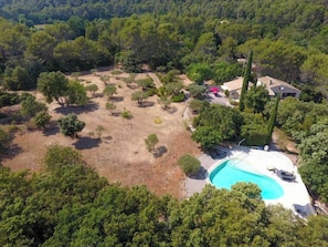 Une vue aérienne d’une propriété dotée d’une piscine, entourée d’arbres et de quelques bâtiments.