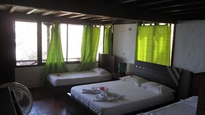 Una camera d'albergo con due letti, un ventilatore e una finestra con tende verdi.