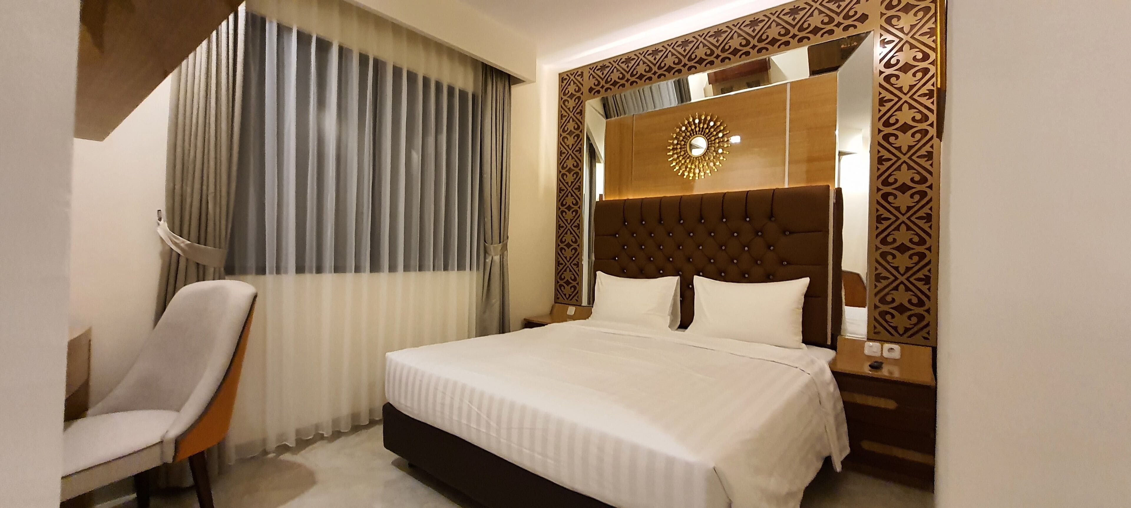 Habitación de hotel con una cama grande, una silla, una mesita de noche y un panel decorativo en la pared.