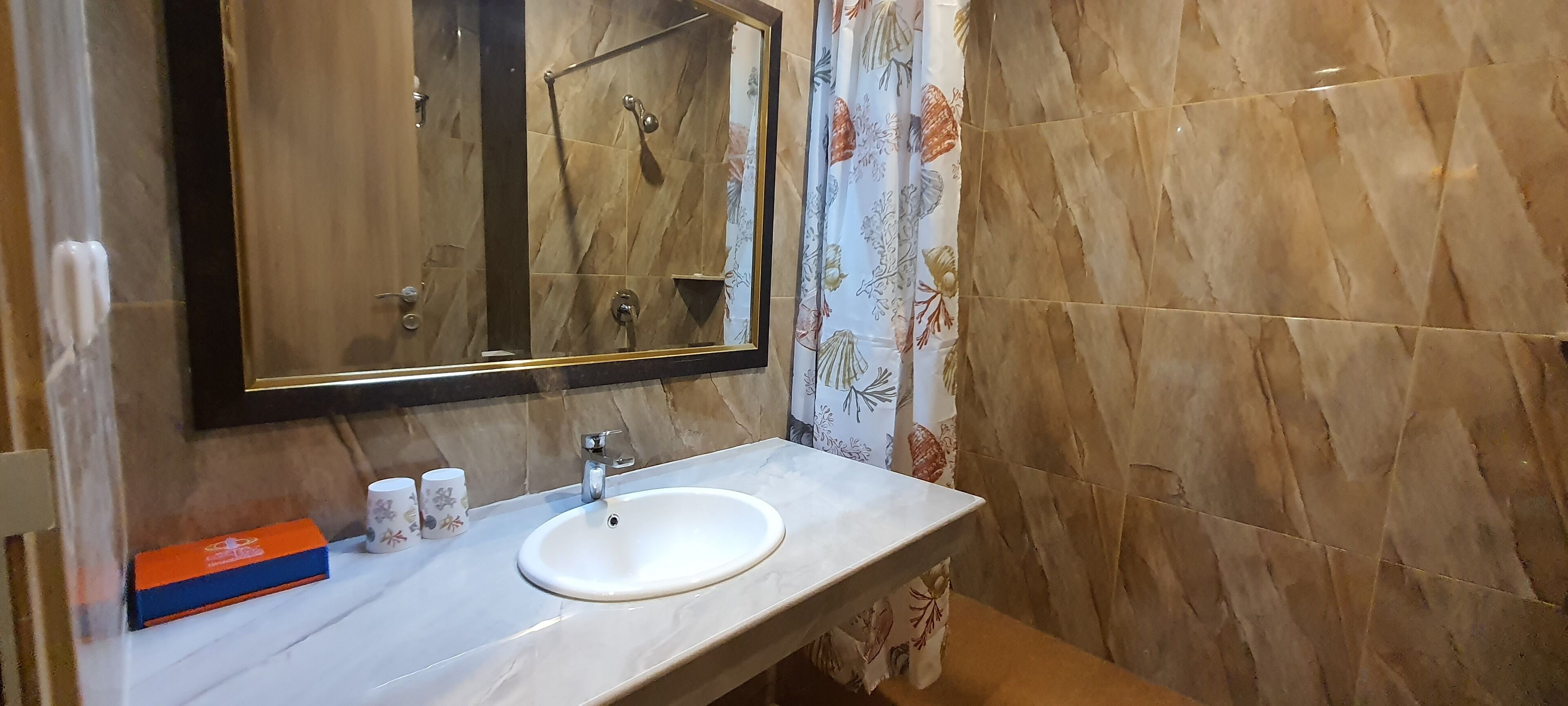 A bathroom with a marble sink, a mirror with a gold frame, and a shower area.
