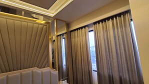 A modern hotel room with a large bed, a window with curtains, and a ceiling light fixture.