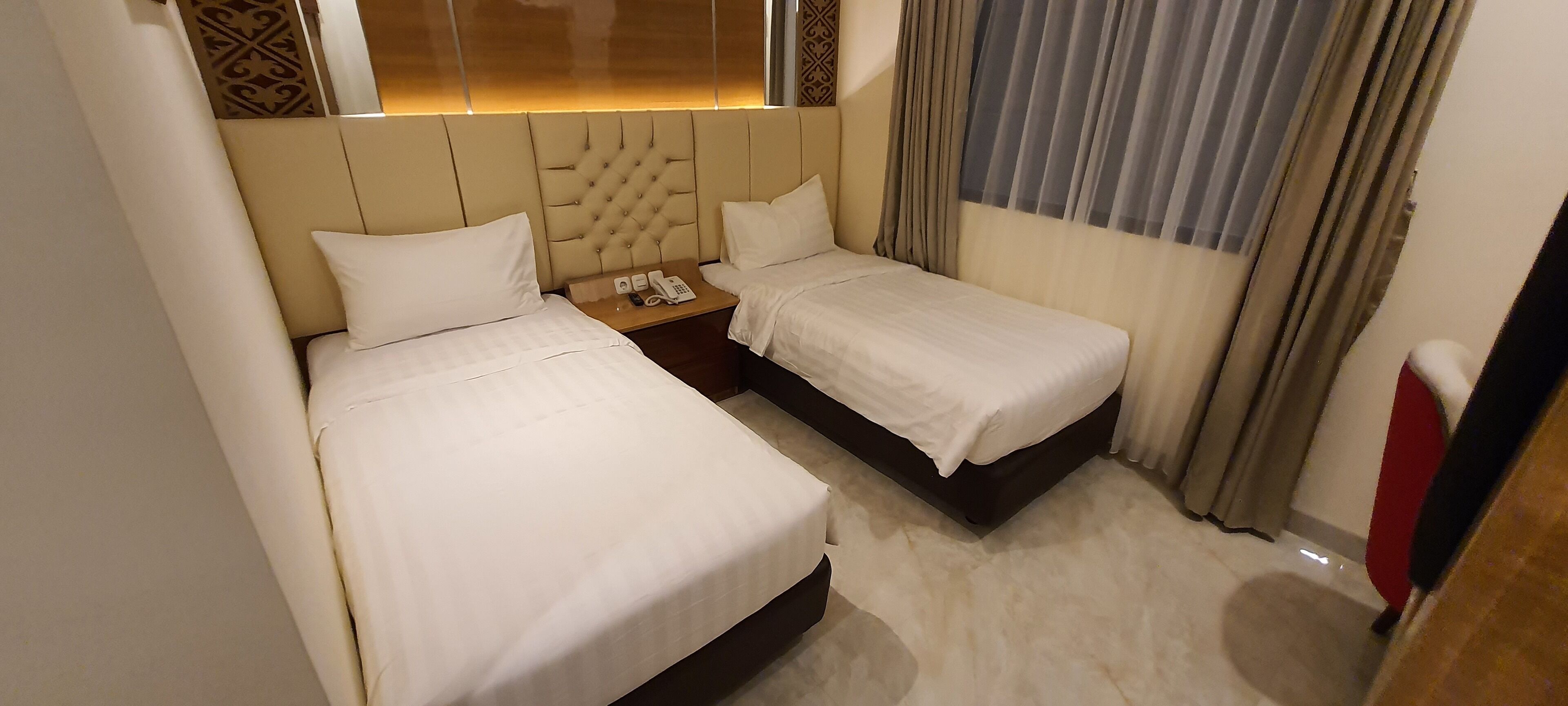 A hotel room with two single beds, a bedside table with a phone, and a decorative headboard.
