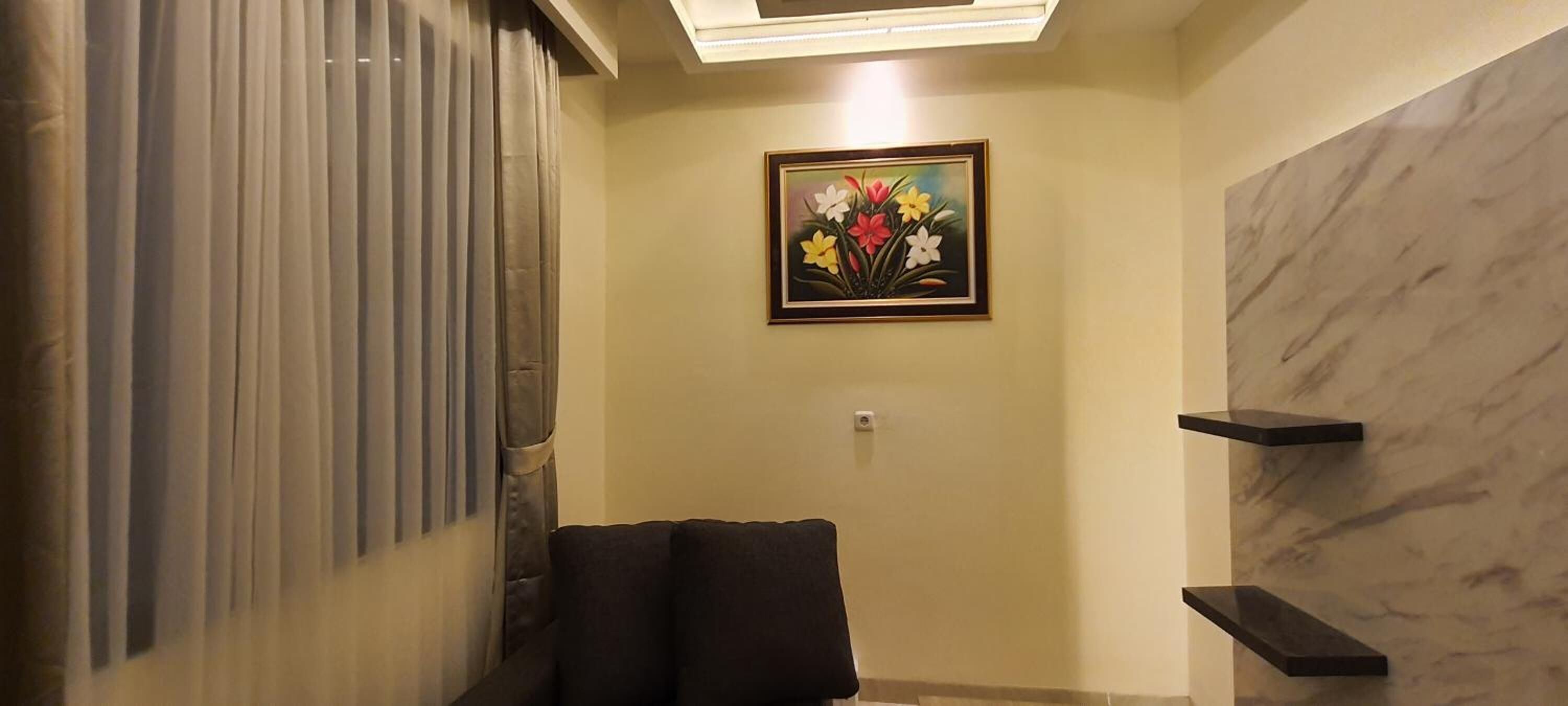 A room with a dark-colored sofa, a painting of flowers on the wall, and a marble-patterned wall.