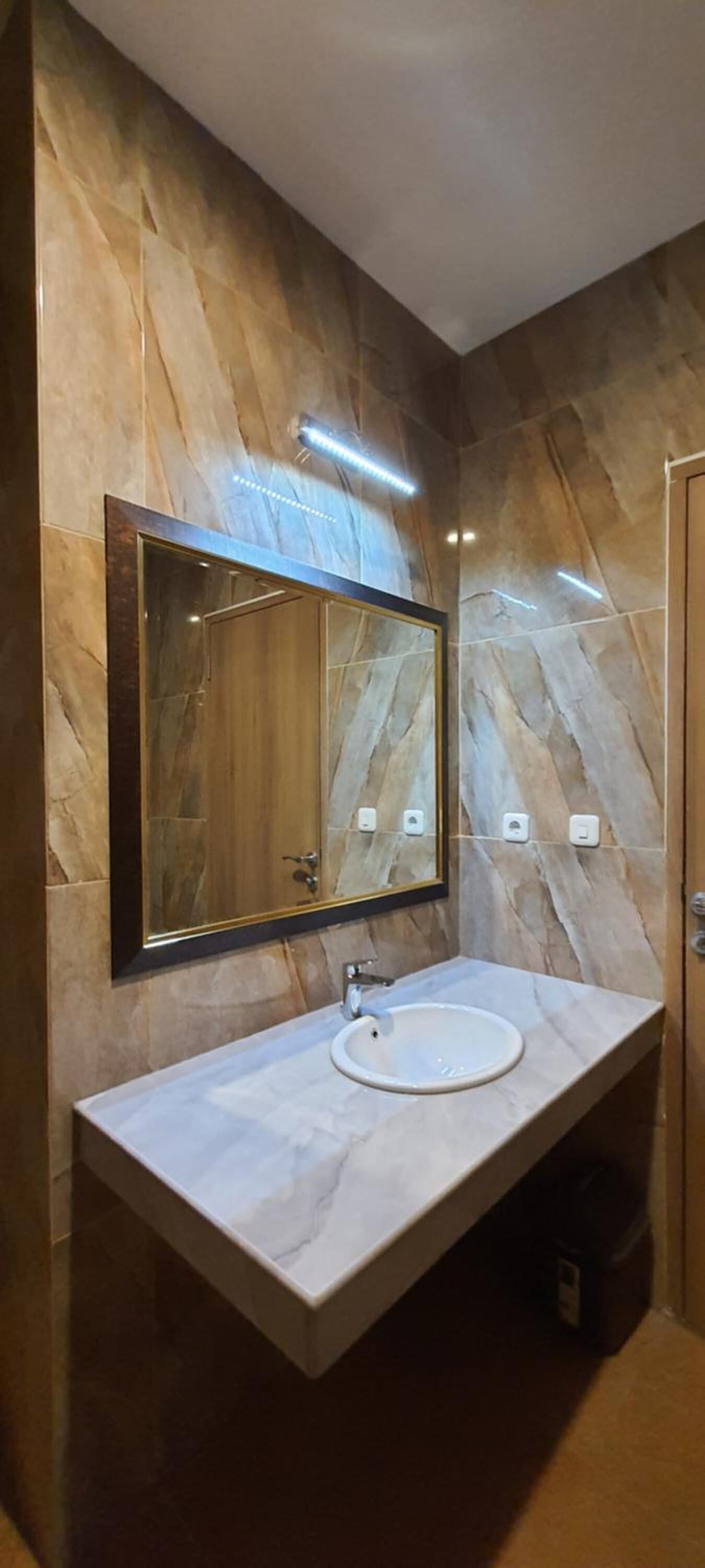 Un baño con tocador de mármol, un espejo grande y una lámpara moderna.