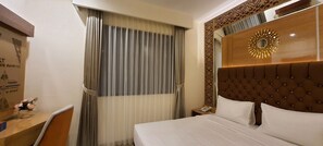 A hotel room with a bed, a bedside table with a phone, a decorative wall panel, and a window with curtains. - Hotel Daily Inn Bandung (Bandung)