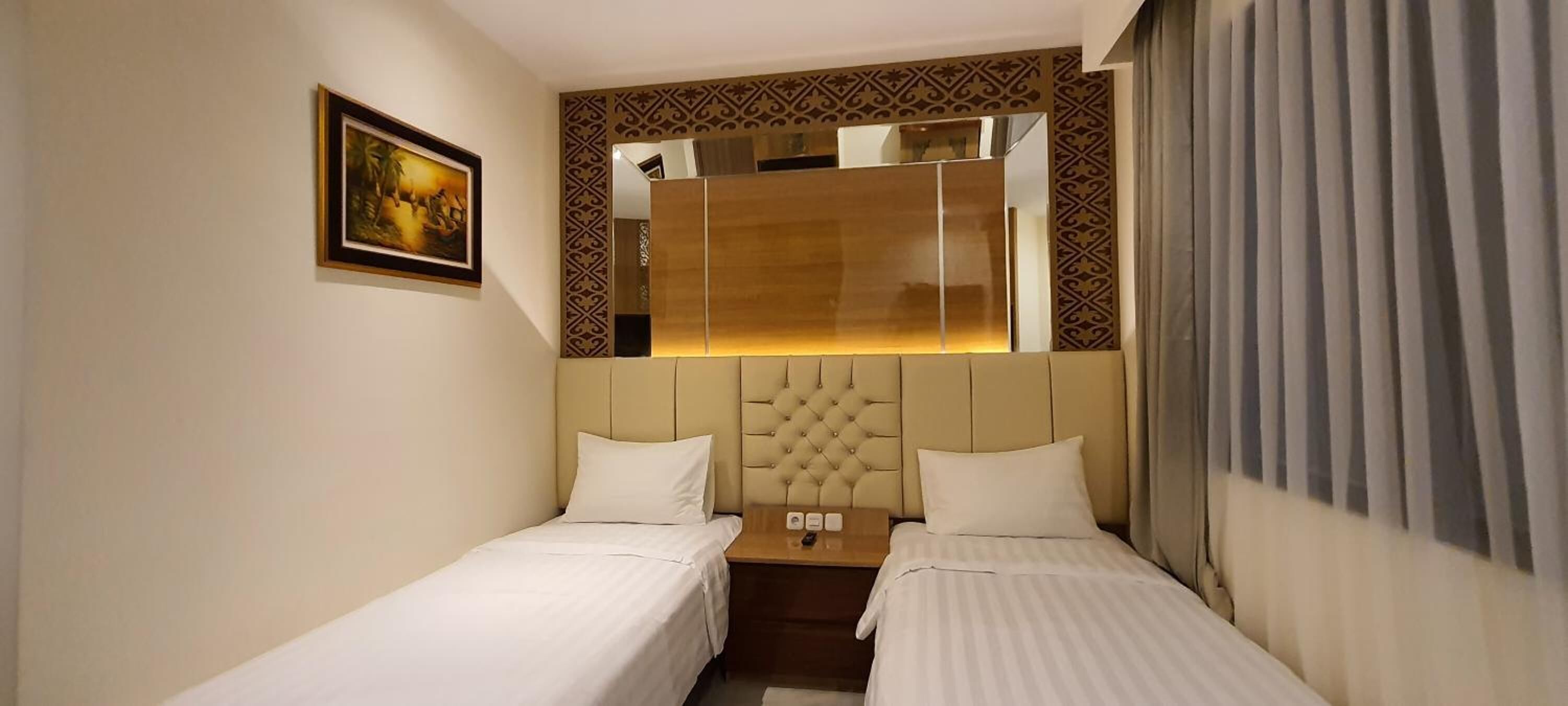 Une chambre d’hôtel avec deux lits simples, un grand miroir, un tableau encadré au mur et une table de chevet avec une lampe.