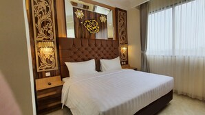 A hotel room with a large bed, a headboard with a mirror, and a view of the outside through sheer curtains.