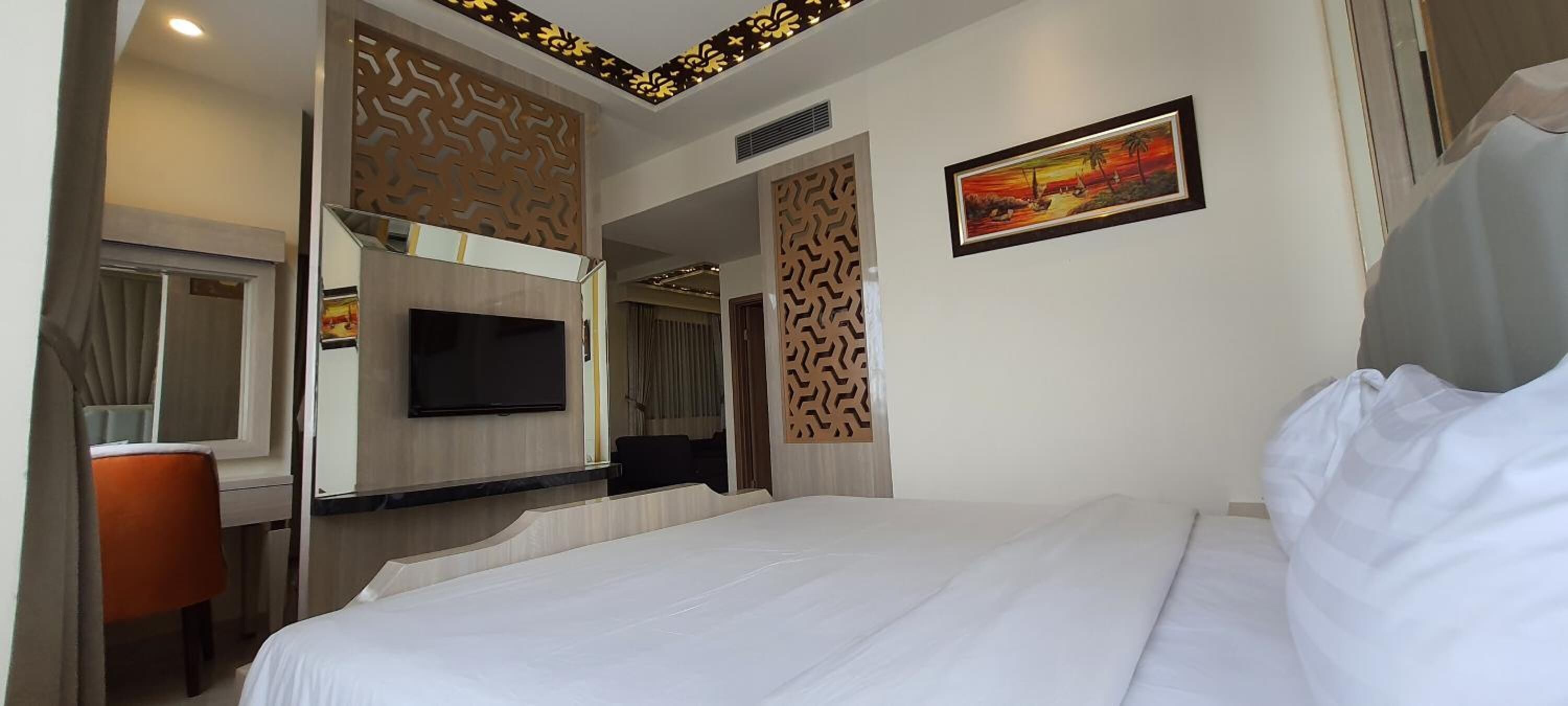 Habitación de hotel con una cama grande, un televisor de pantalla plana montado en la pared, un escritorio con una silla y un panel decorativo en la pared.