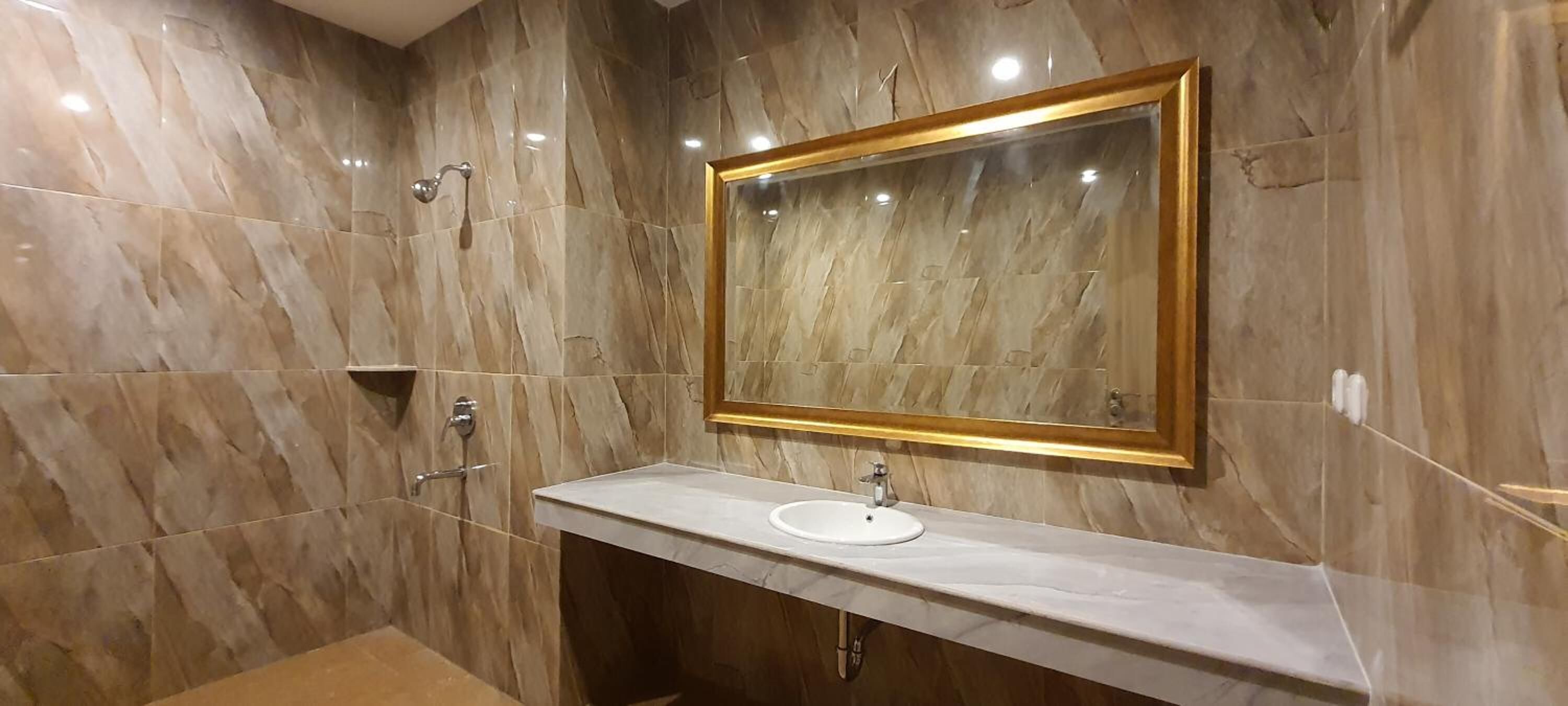 Un baño con pared de mármol, un lavabo con espejo y una ducha.