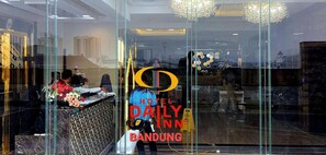 A hotel reception desk with a glass partition, a floral arrangement, and a sign for Hotel Daily Inn Bandung. - Hotel Daily Inn Bandung (Bandung)