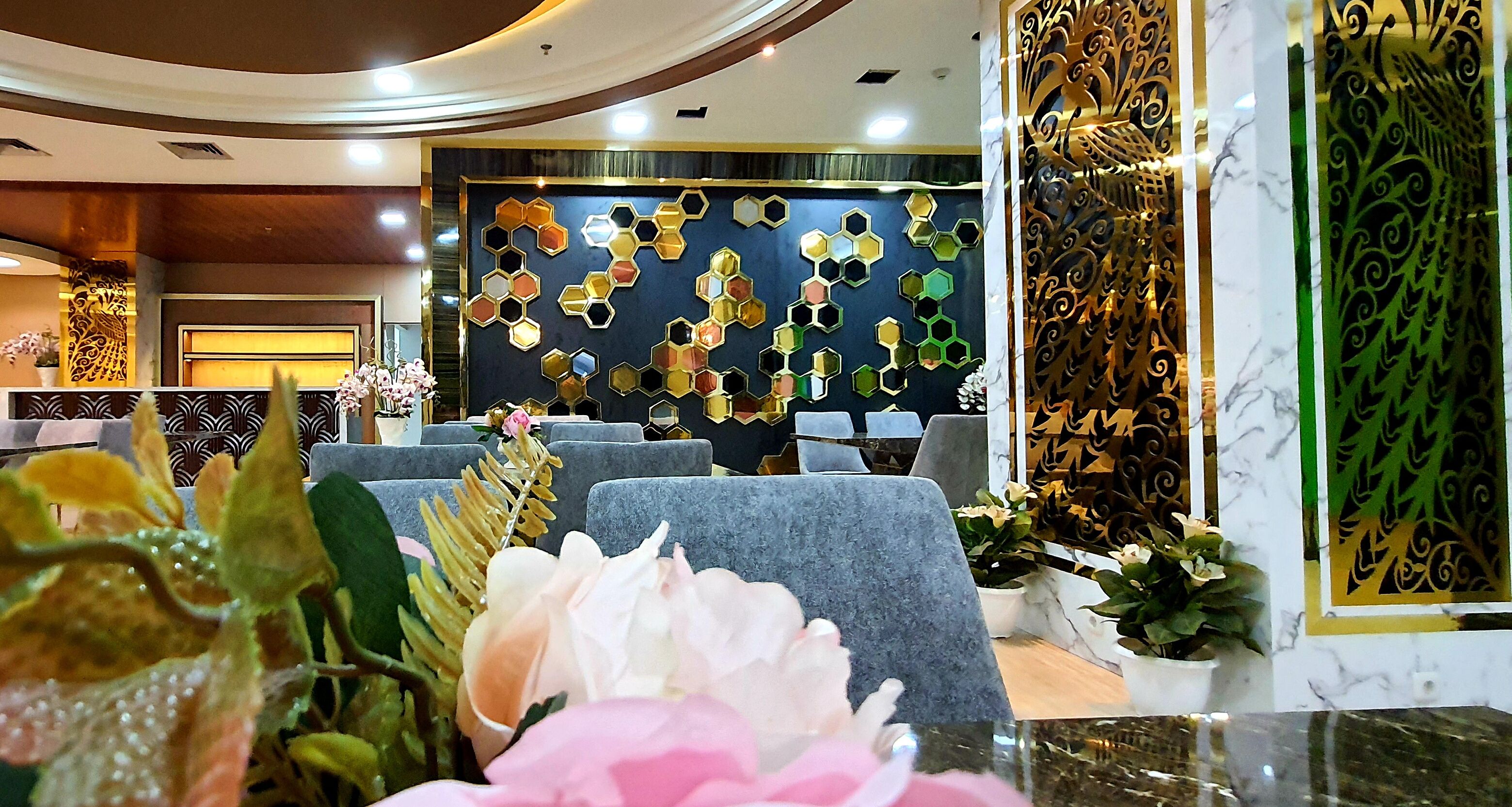A hotel lobby with a modern design, featuring a seating area with grey sofas, a decorative wall with hexagonal mirrors, and a marble reception desk.