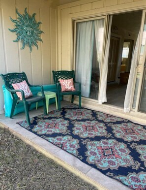 A covered porch with two green chairs and a patterned rug.