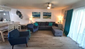 Een woonkamer met een eethoek, een zithoek, een salontafel en een plafondventilator.