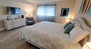 A bedroom with a bed, a dresser, a chair, a TV, and a window with curtains.