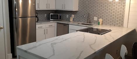 Una cocina moderna con armarios blancos, un refrigerador de acero inoxidable, un microondas y una encimera de mármol.