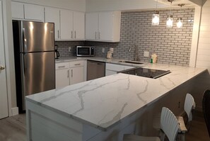 A modern kitchen with white cabinetry, a stainless steel refrigerator, a microwave, and a marble countertop.