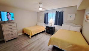 Een slaapkamer met twee bedden, een televisie, een dressoir en een klein kastje.