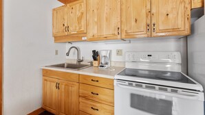 A kitchen with wooden cabinets, a stainless steel sink, a white stove, and a coffee maker. - Comfy Country Condo - East (Gallatin Gateway)
