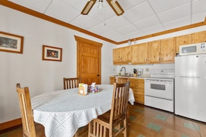 Une cuisine avec des meubles de rangement en bois, un réfrigérateur blanc, une cuisinière et une table à manger avec des chaises.