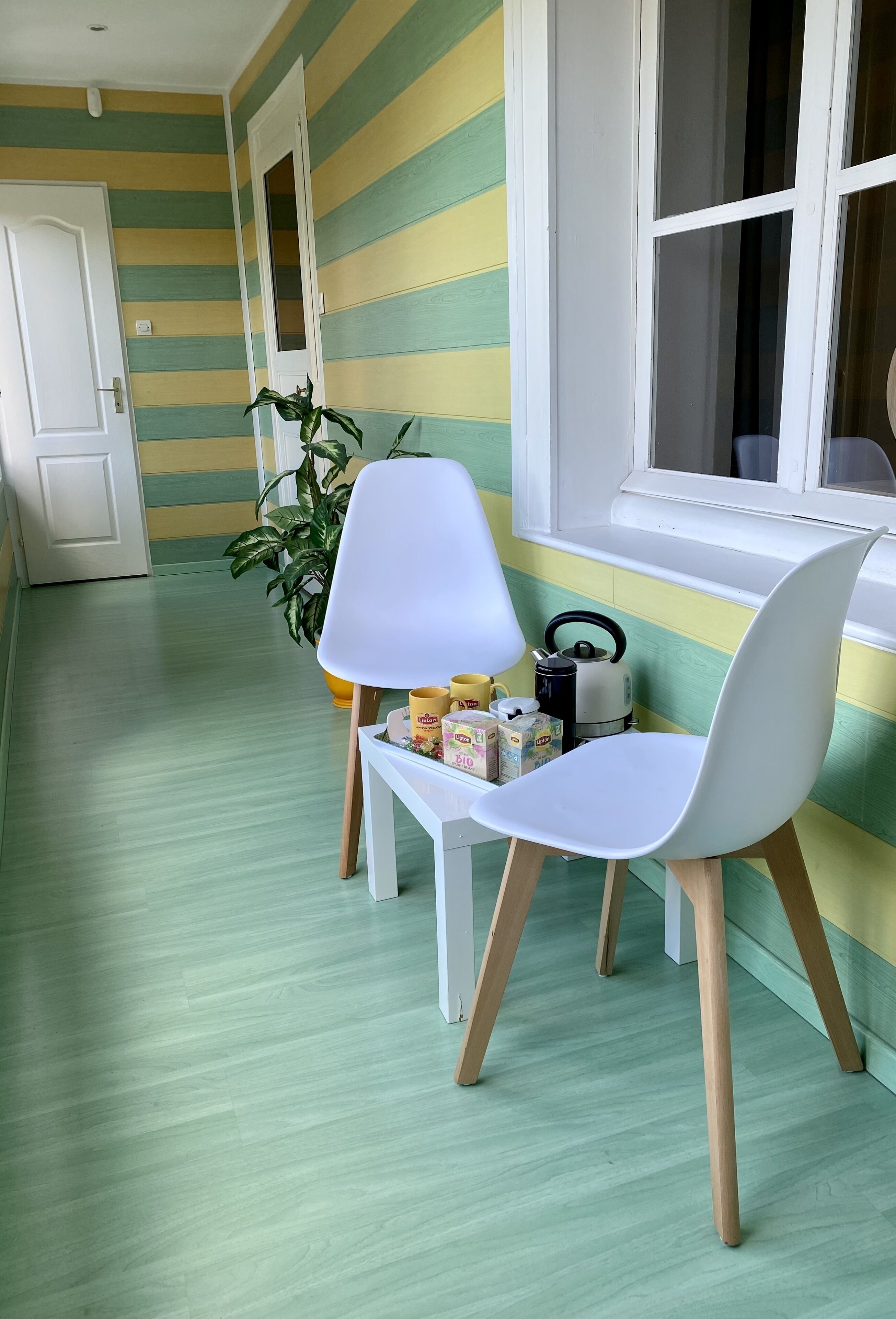 Una habitación con una pared a rayas, una silla blanca, una mesita y una ventana.