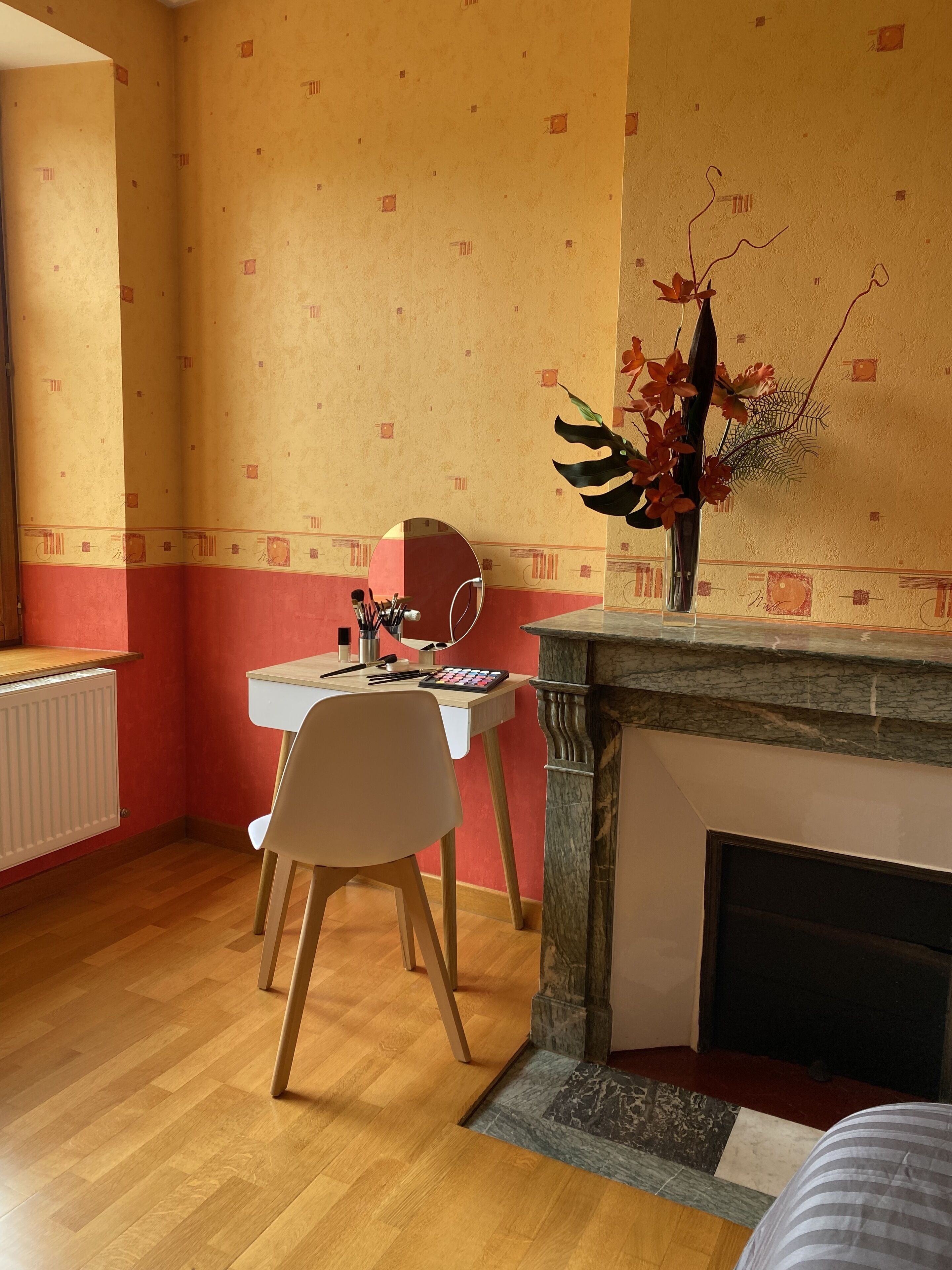 Ein Zimmer mit Holzboden, einem weißen Schreibtisch mit Stuhl, einer Blumenvase und einem Kamin.