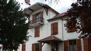 Een gebouw met twee verdiepingen, houten luiken, een balkon en een overdekte ingang.