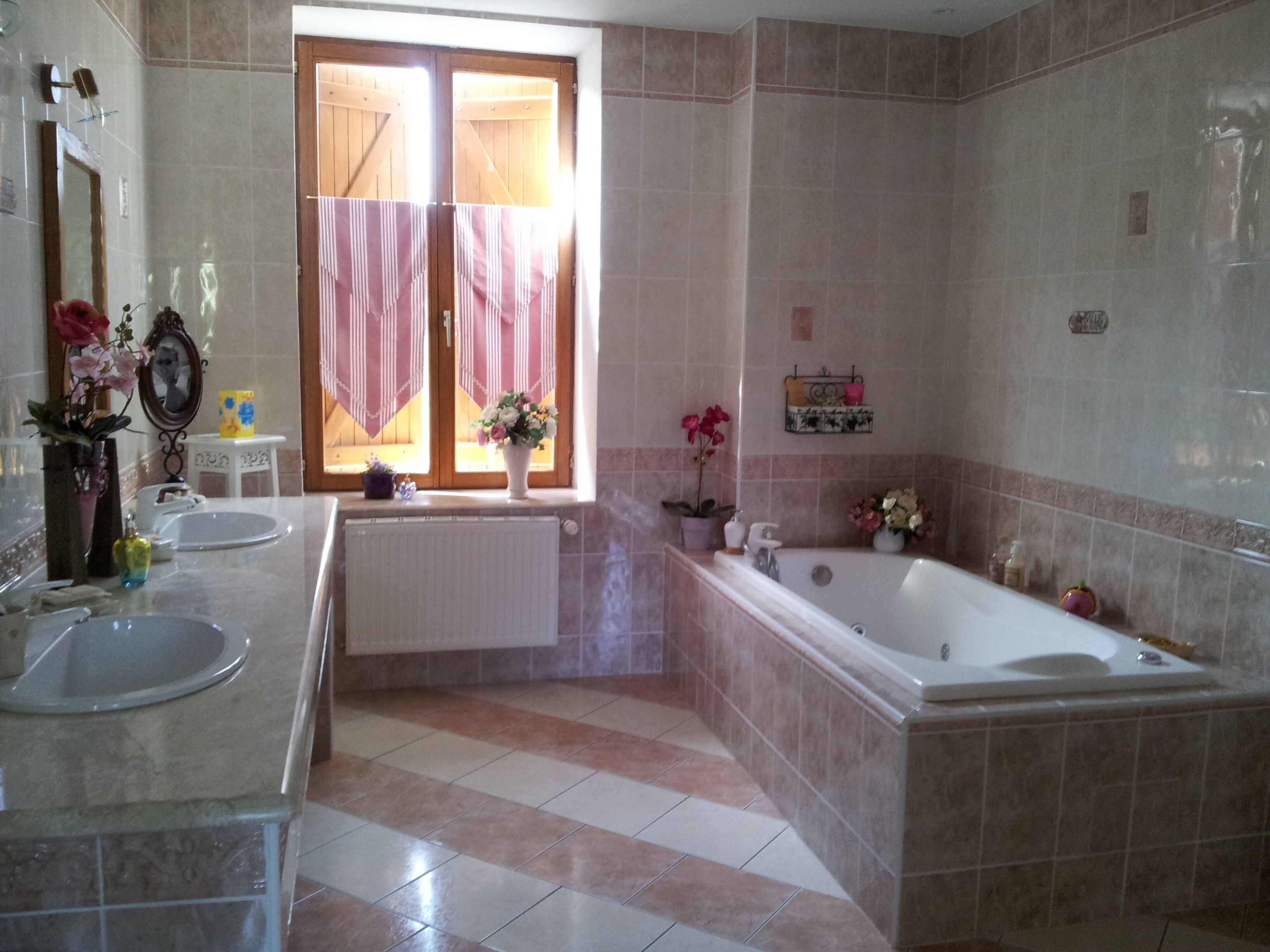 A bathroom with a bathtub, two sinks, a window with a pink curtain, and a mirror.