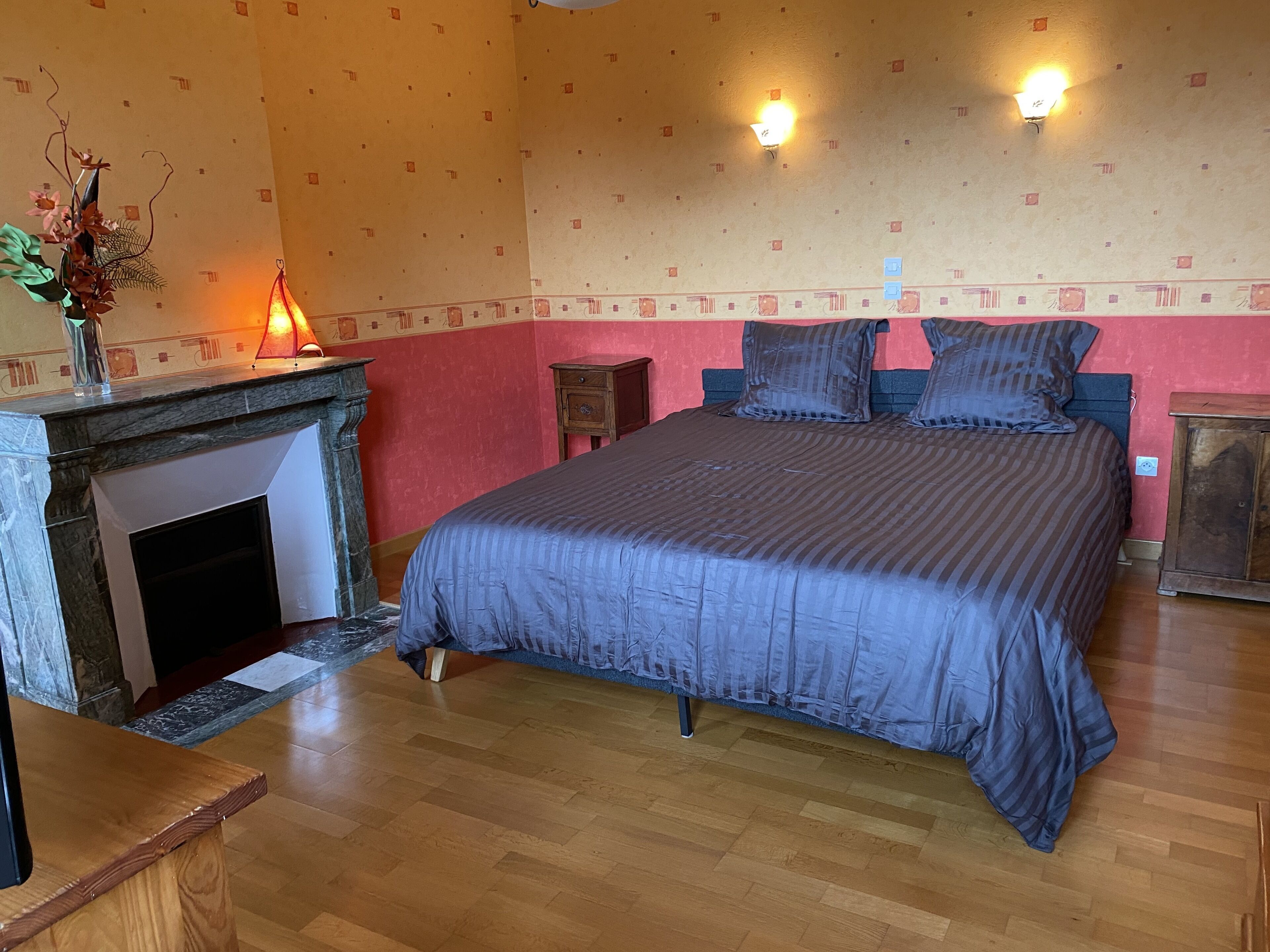 Ein Schlafzimmer mit Bett, Kamin, Nachttisch und einer Wandleuchte.