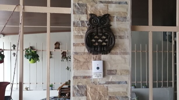 Une pièce avec un mur en pierre, une décoration en forme de hibou en bois et une table recouverte d’une nappe à motifs floraux.