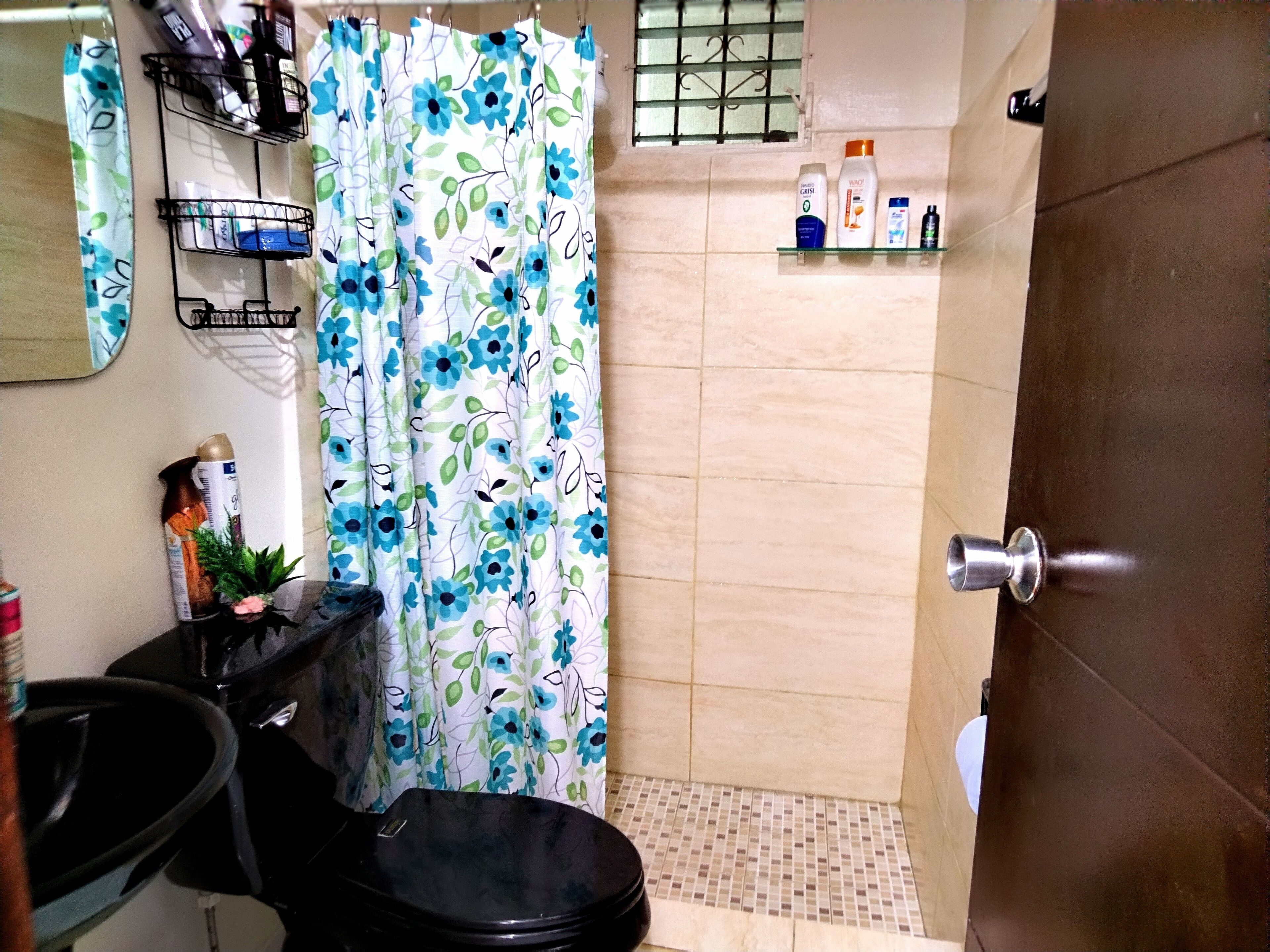 A bathroom with a shower curtain, a toilet, a sink, and toiletries on a shelf.