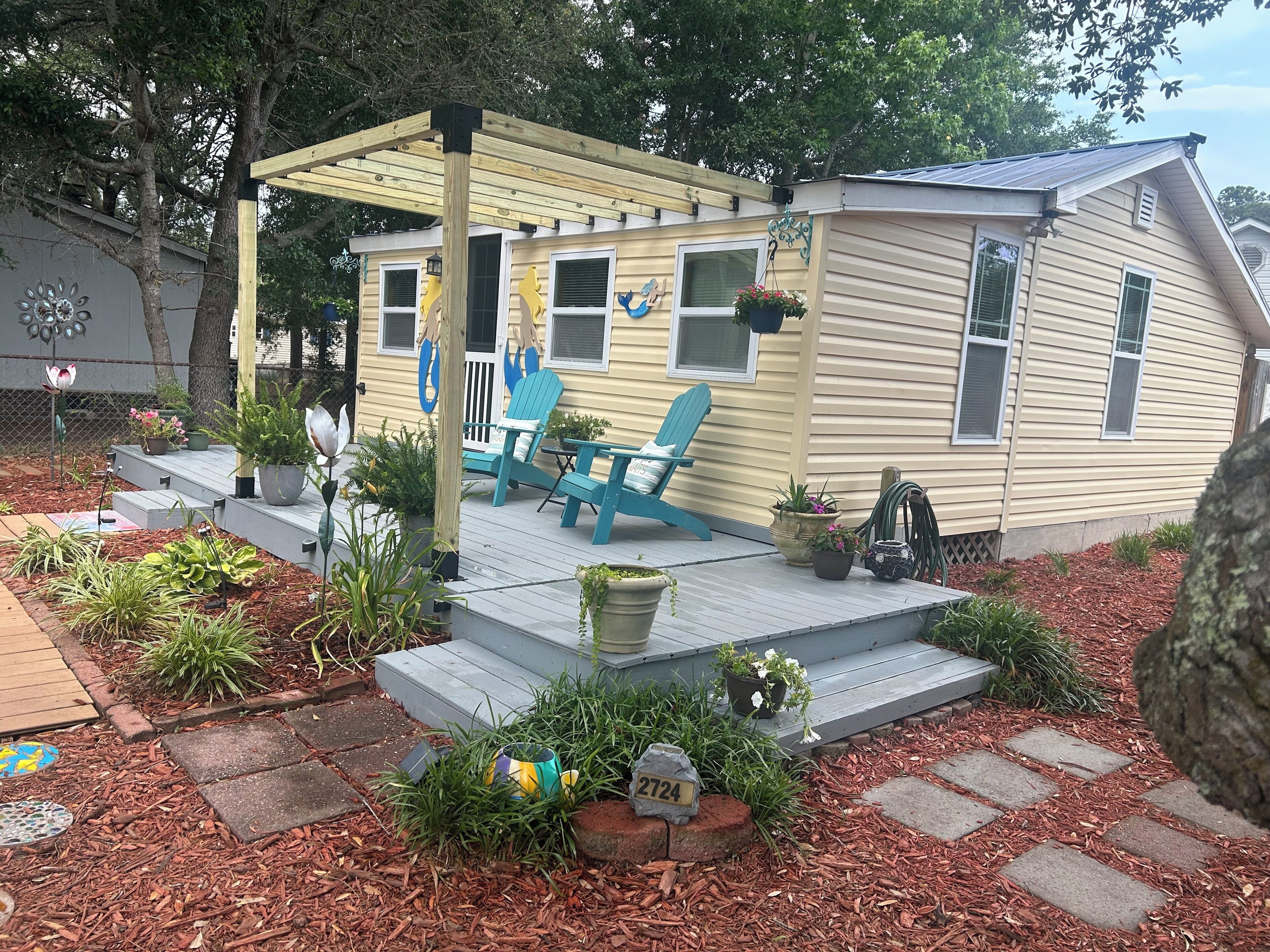 A mobile home with a porch, blue Adirondack chairs, and potted plants.