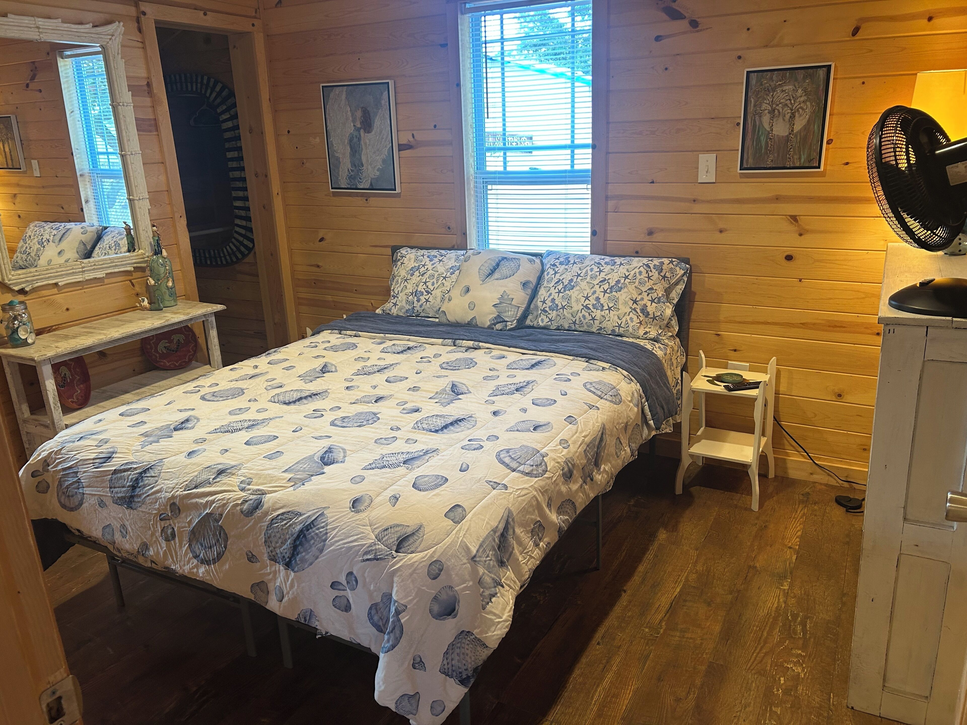 Camera da letto in una baita di legno, con un letto, un comodino e una ventola.