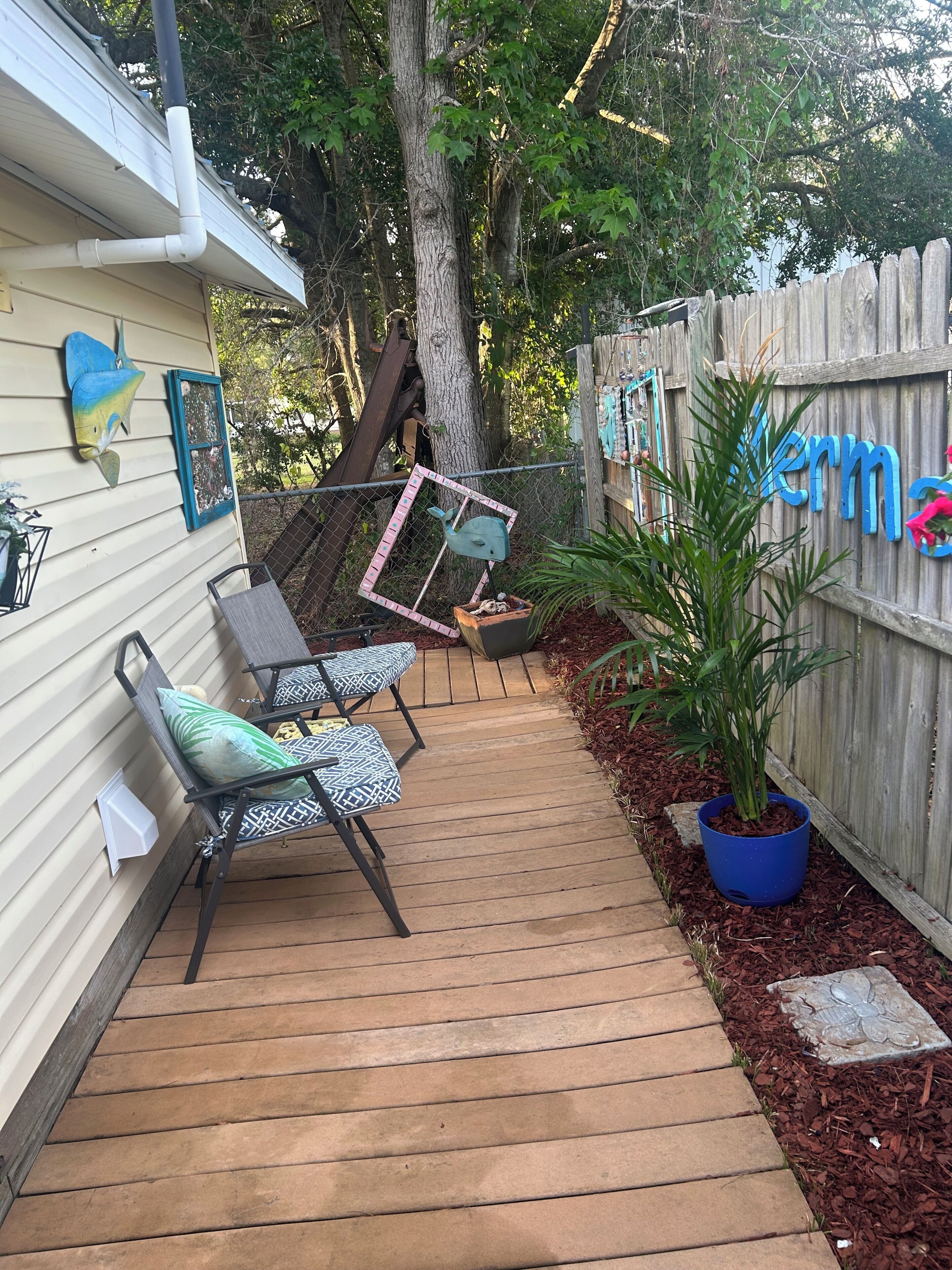 A wooden deck with outdoor furniture, a blue potted plant, and a wooden fence with a sign.