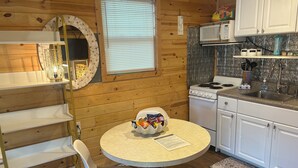 A kitchen with wooden walls, a round table, a white chair, a stove, and a sink. - Pet Friendly Separate Fee, enjoy fenced in yard, outdoor shower, fire pit (Holden beach)