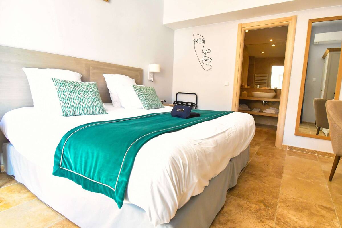 Une chambre d’hôtel avec un lit, un bureau, une chaise et une salle de bain visible à travers une porte ouverte.