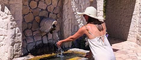 Una mujer sirve agua de una fuente de piedra en una cuenca.