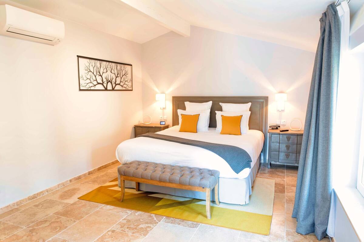 Une chambre d’hôtel moderne avec un grand lit, deux tables de chevet, un banc et un climatiseur fixé au mur.