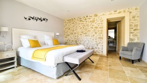 A bedroom with a large bed, a bedside table, a chair, and a stone wall. - Domaine Ribiera, Hotel 5 Etoiles, SPA & Golf - Forcalquier (Niozelles)
