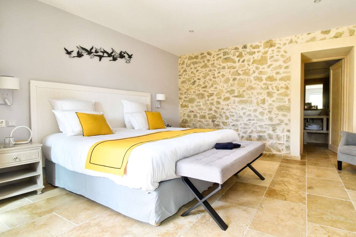 Une chambre avec un grand lit, une table de chevet, une chaise et un mur en pierre.