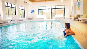 An indoor swimming pool with clear blue water, wooden beams on the ceiling, and white lounge chairs around the pool. - Domaine Ribiera, Hotel 5 Etoiles, SPA & Golf - Forcalquier (Niozelles)