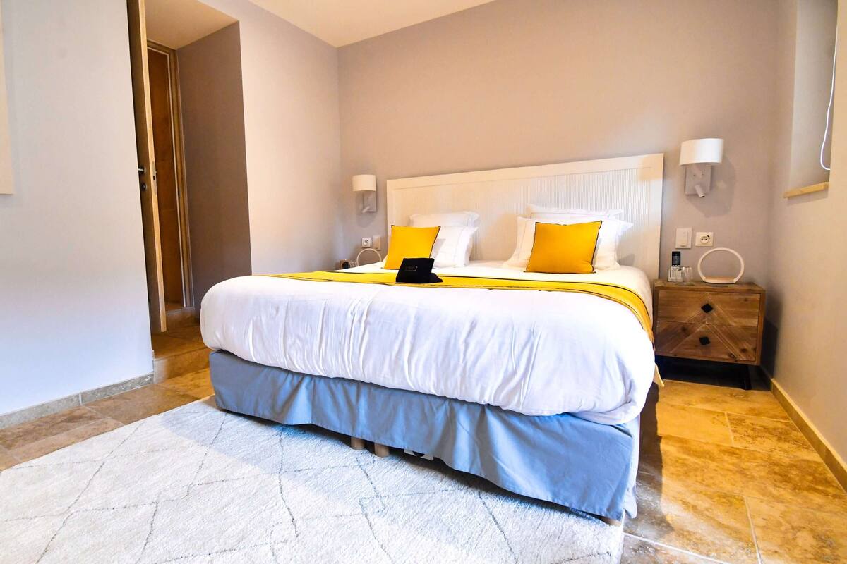 Une chambre à coucher comprenant un lit, des tables de chevet, une commode, une lampe et un luminaire fixé au mur.