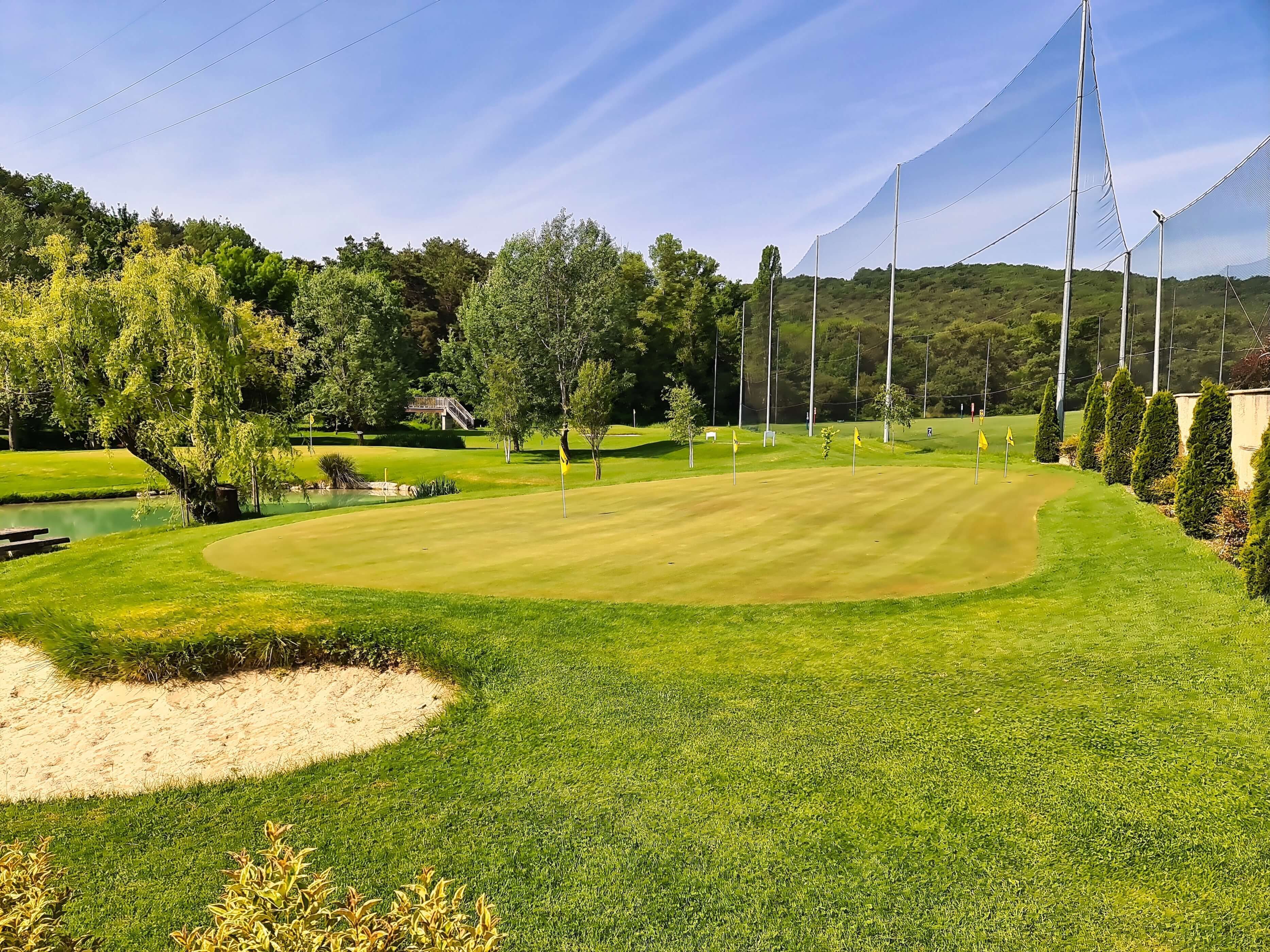 A well-maintained golf course with sand bunkers, a pond, and a clear sky.