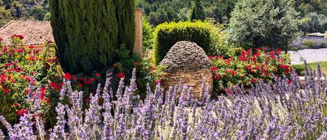 Un jardín con lavanda, flores rojas y una estructura de piedra.