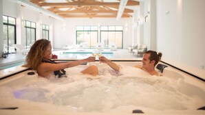 A couple in a hot tub with a pool view, wooden beams, and large windows. - Domaine Ribiera, Hotel 5 Etoiles, SPA & Golf - Forcalquier (Niozelles)