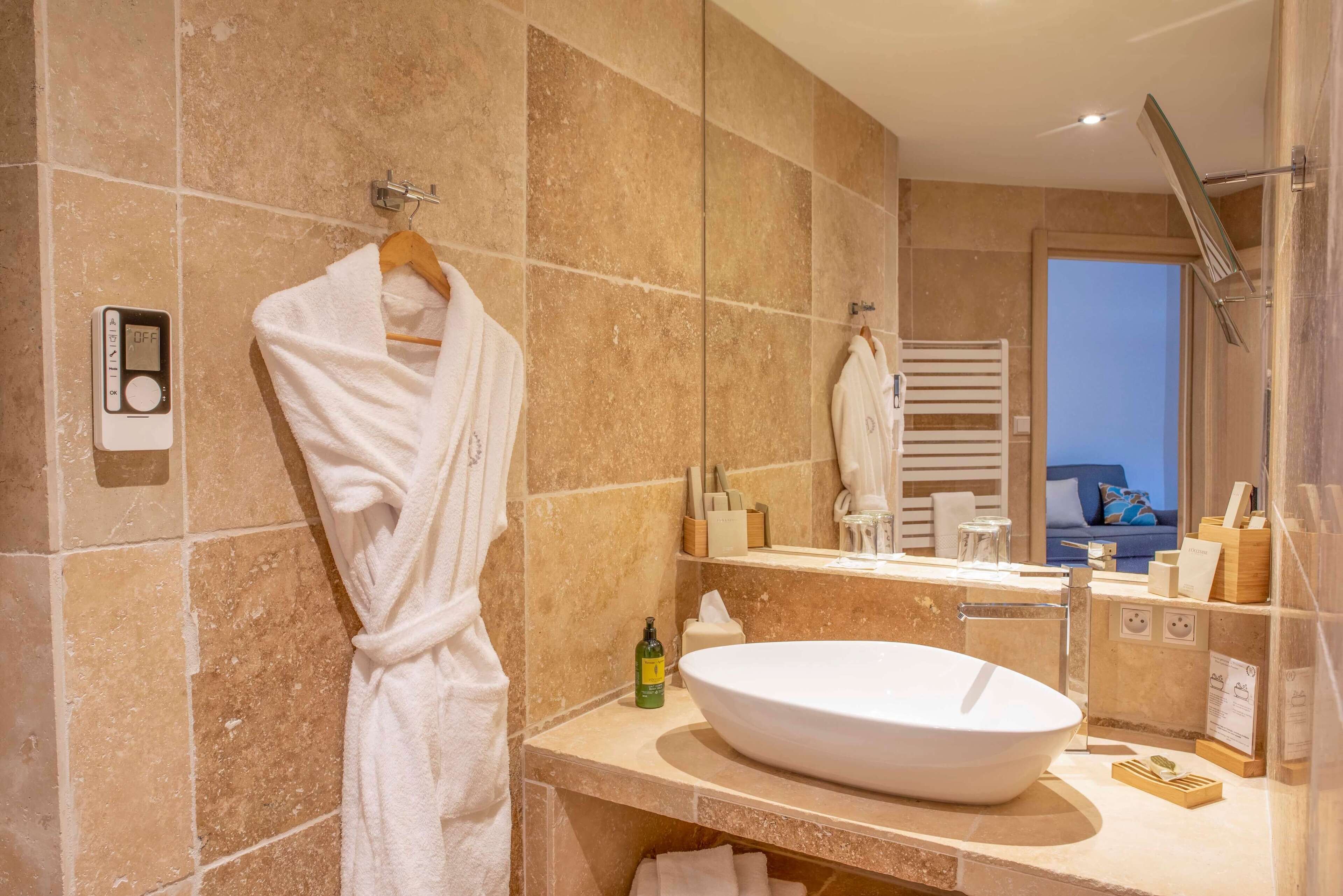A modern bathroom with a large oval sink, a towel rack with a white robe, and a scale on the wall.