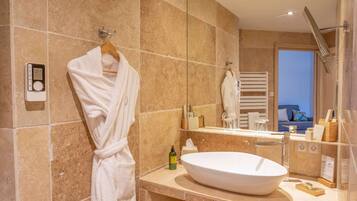 A modern bathroom with a large oval sink, a towel rack with a white robe, and a scale on the wall.