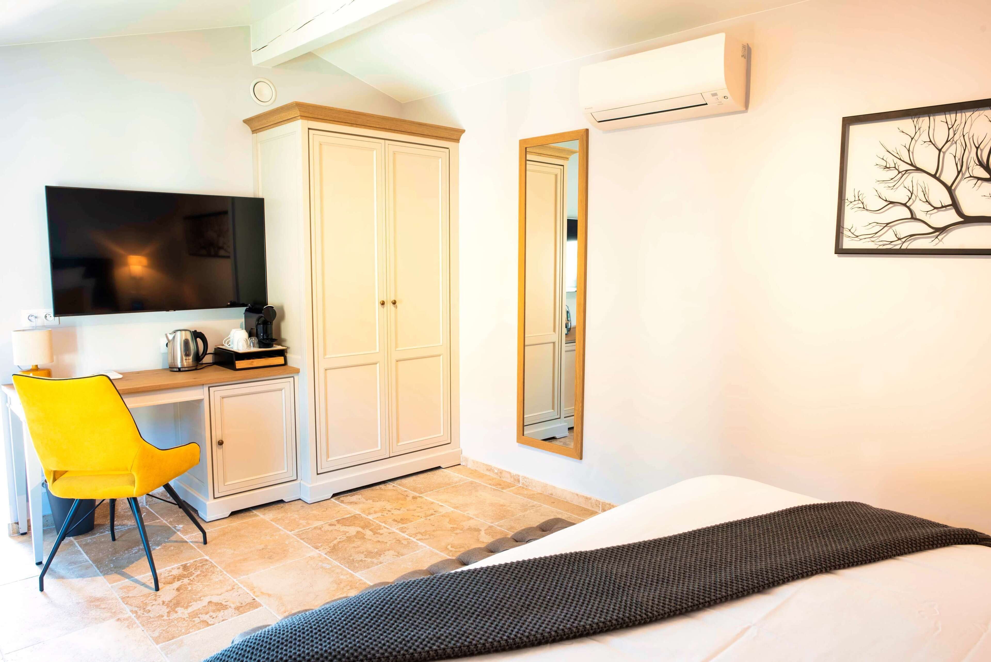 A hotel room with a bed, a desk with a chair, a TV, and a wardrobe.