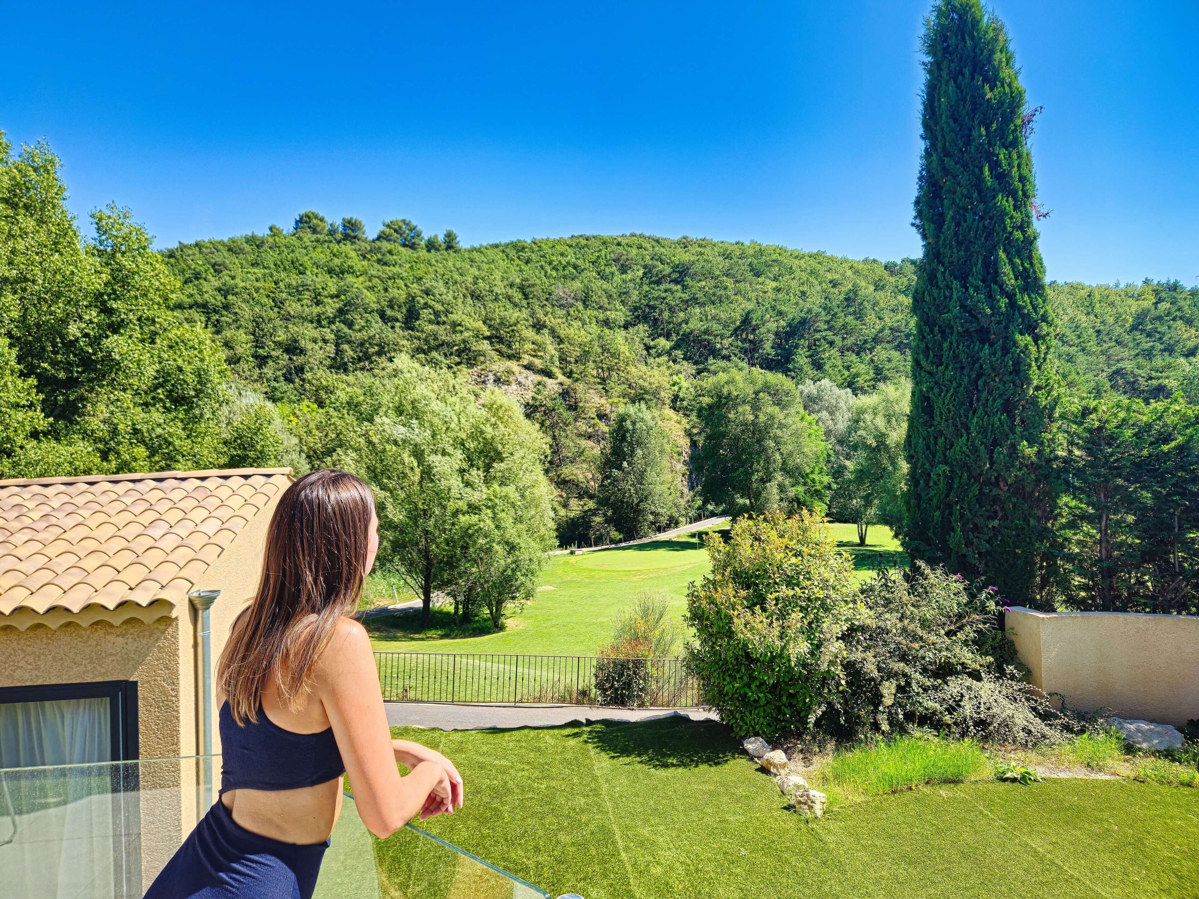 A view from a balcony overlooking a lush green landscape with trees and hills.