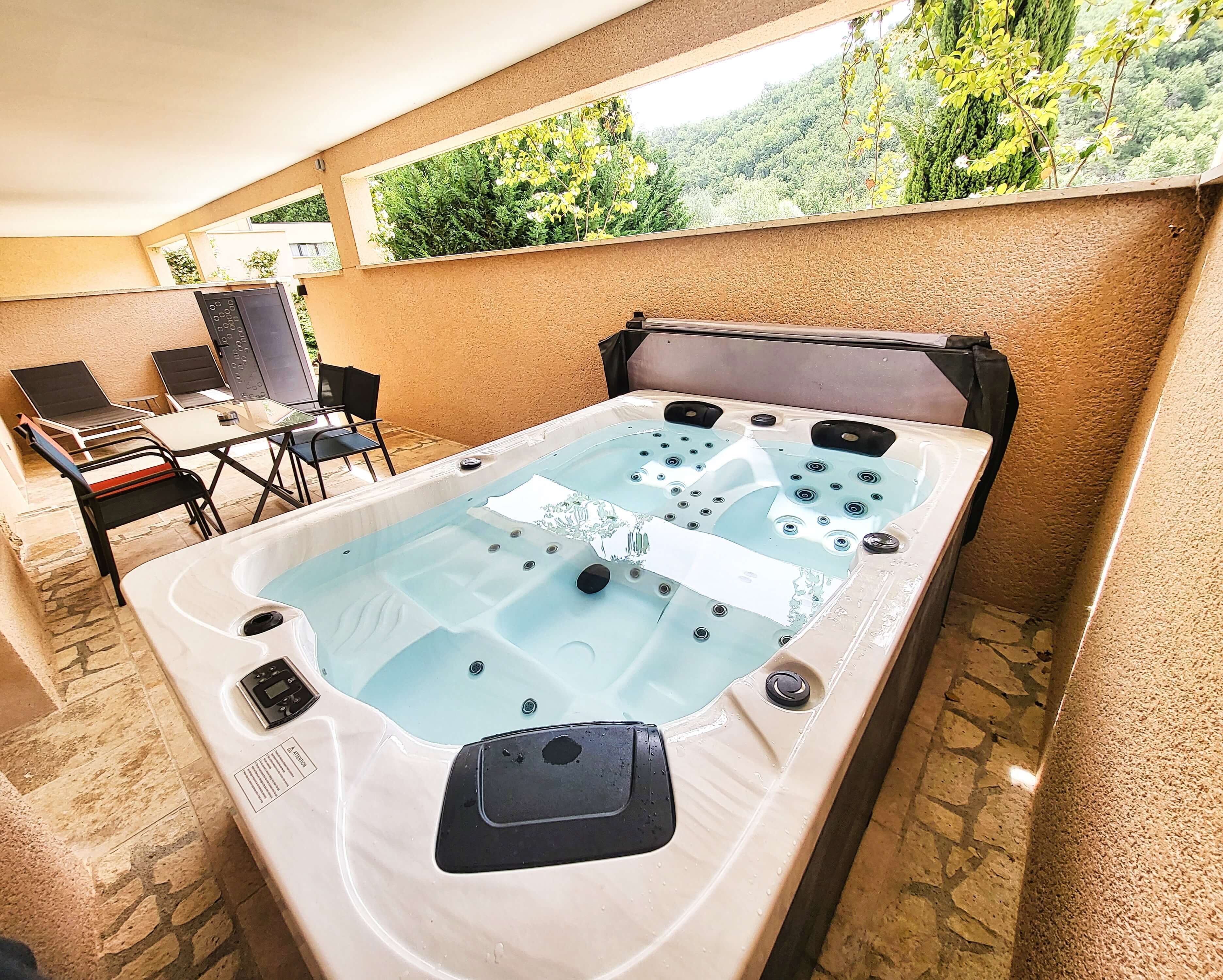 Ein Whirlpool mit Bedienfeld, ein Tisch mit Stühlen und Blick auf Grün hinter einem Fenster.