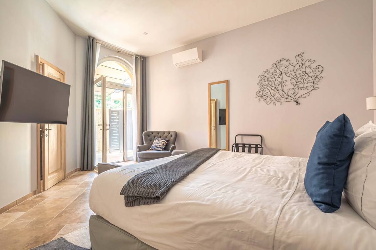 Une chambre dotée d’un grand lit, d’un téléviseur à écran plat, d’un miroir et d’une œuvre d’art murale.